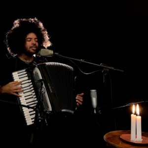 Imagem do artista Mestrinho e sua sanfona com duas velas acesas, reprodução do clipe da canção Navegando Juntos